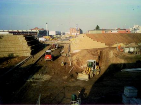 Baugrube mit Baufahrzeugen und gestapelten Materialien im Hintergrund.